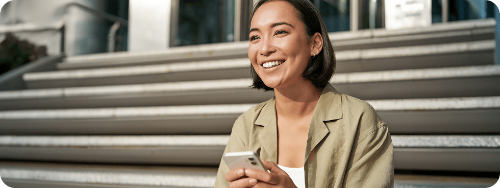 Sara, smiling outdoors with her phone in natural light